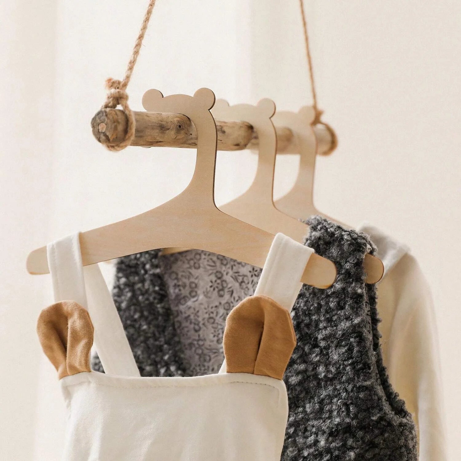 Bear-shaped wooden baby clothes hangers on a rustic rope rack, light beige wood