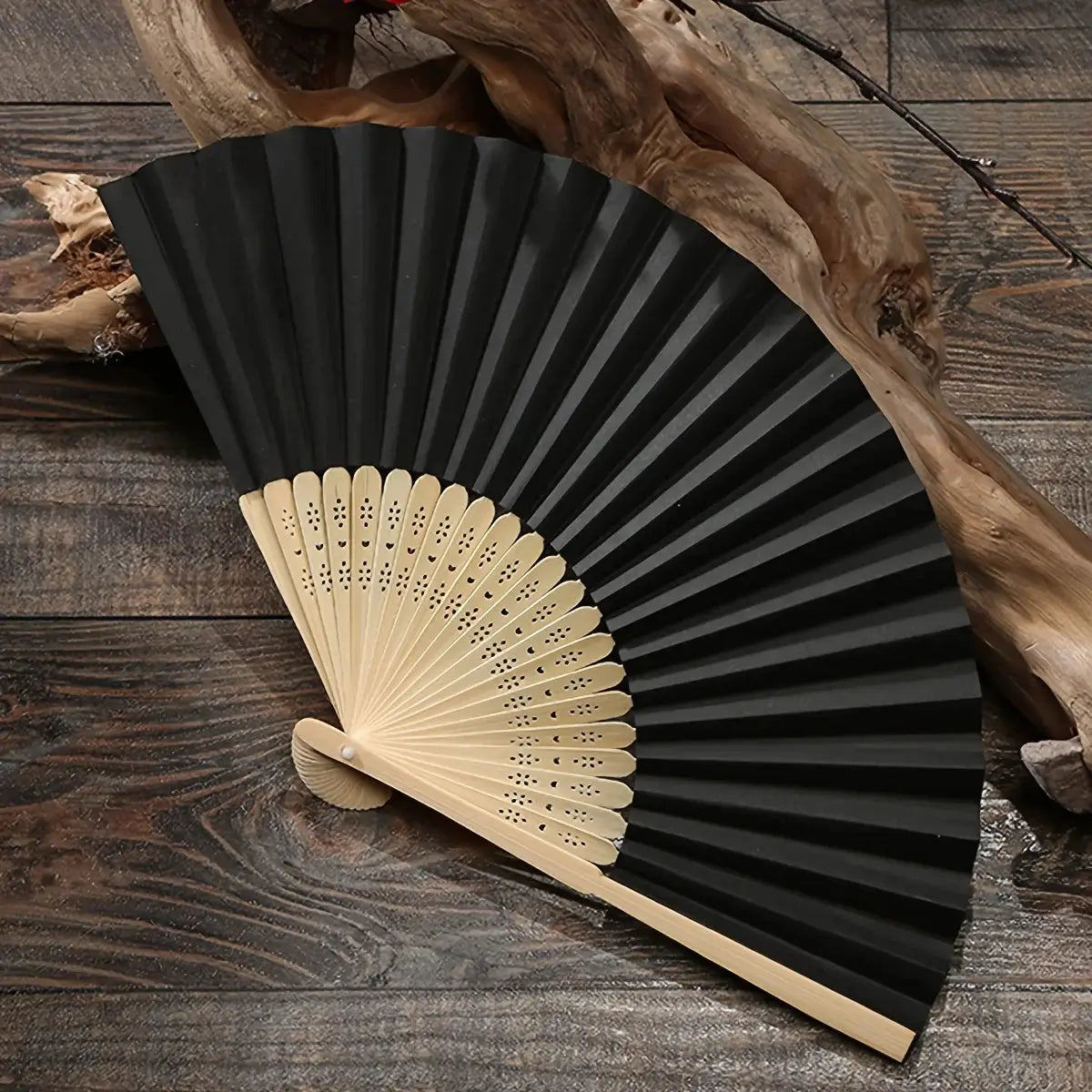 Black bamboo hand folding fan with pale wood ribs, displayed on a dark wooden surface.