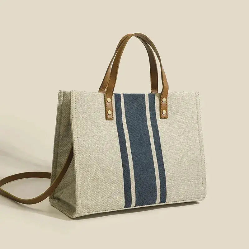 Canvas stripe tote bag with brown top handles and shoulder strap; beige canvas with a dark blue central stripe