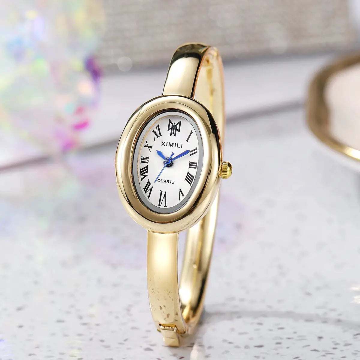 Gold-tone wristwatch for women by XIMILI with oval dial, Roman numerals and blue hands
