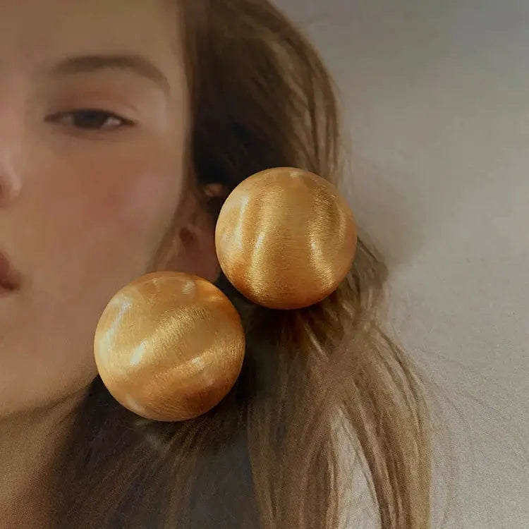 Pair of gold-tone brushed metal ball earrings worn by model, large statement studs