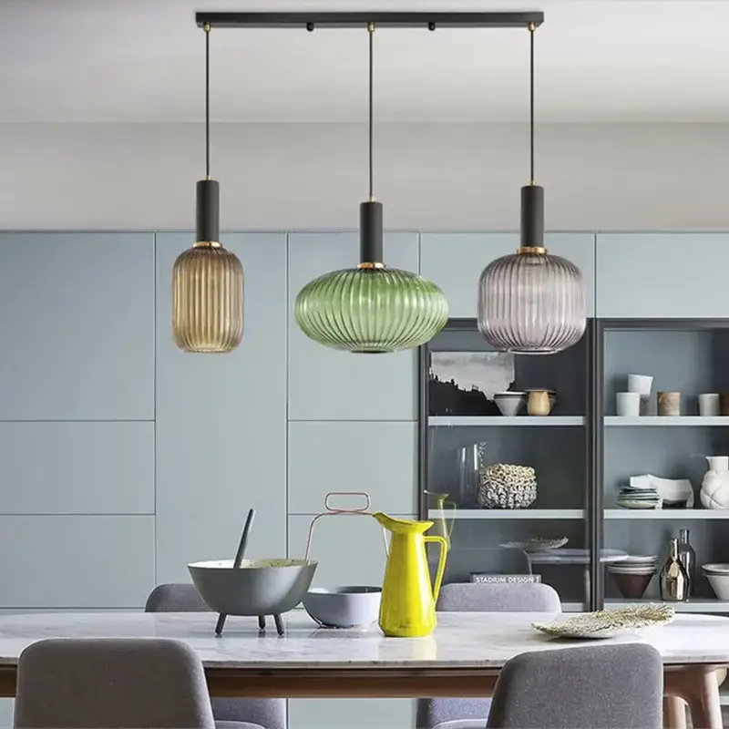 Three glass pendant lights in beige, green and gray hanging over a dining table in a modern kitchen.
