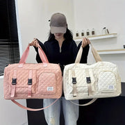 Two diamond-quilted nylon duffle bags in pink and ivory with front zip pockets and buckle straps.