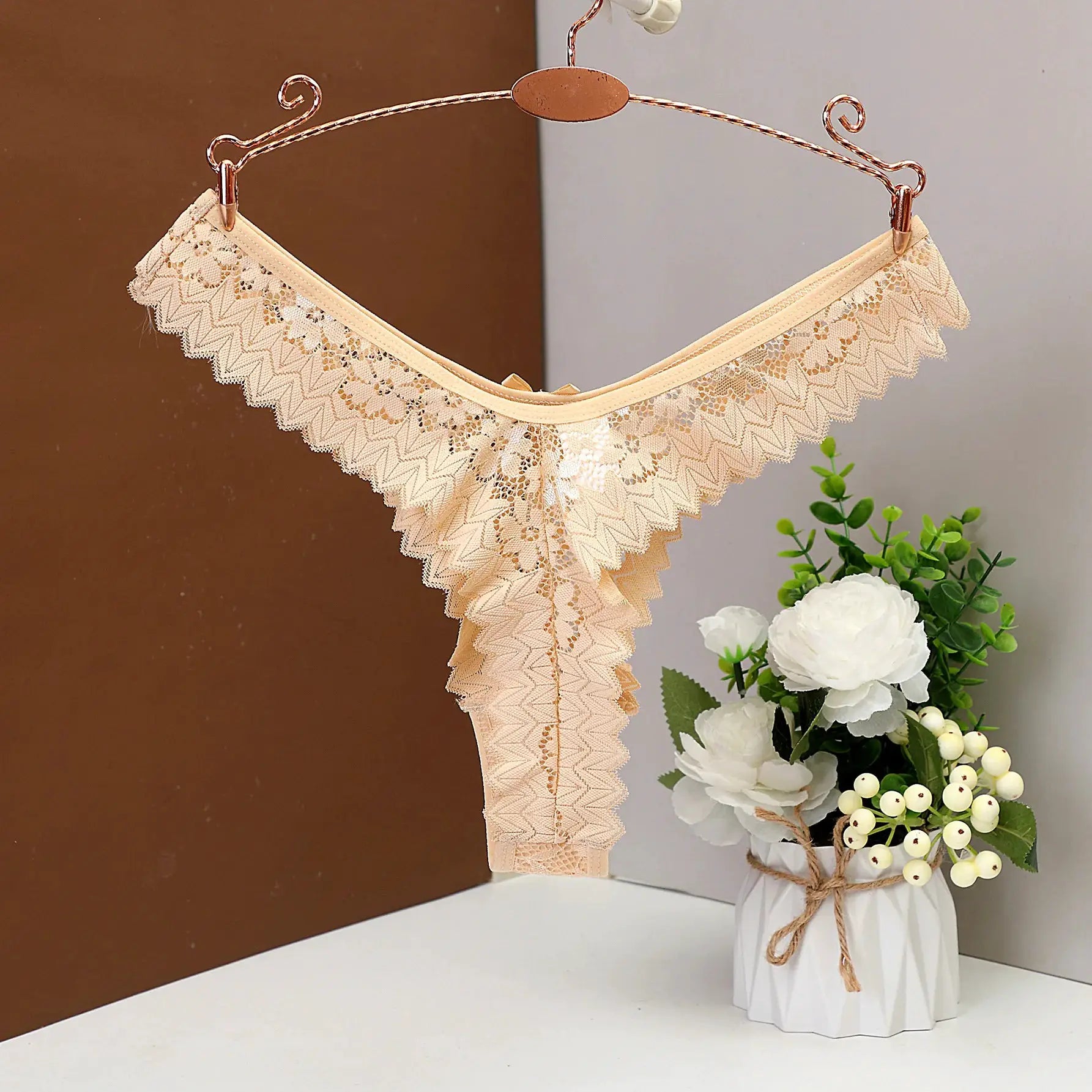 Beige lace thong underwear, low-waist lingerie with scalloped edges displayed on a copper hanger.