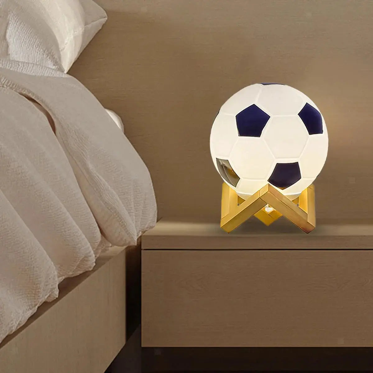 Soccer ball night light on a gold geometric stand atop a bedside table.