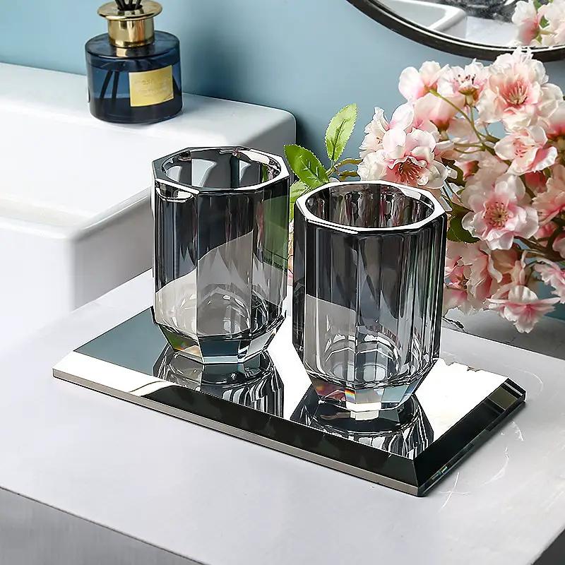 Glass bathroom set with two blue-tinted crystal cups on a mirrored tray.