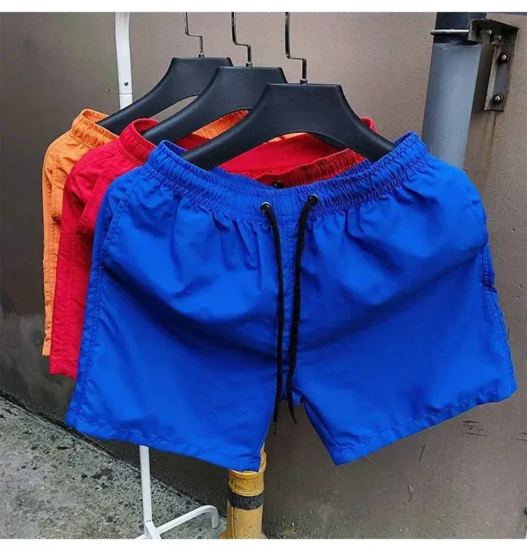 Men's blue swim shorts with black drawstrings; four color variants on hangers.