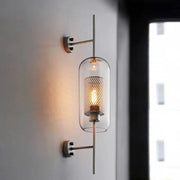 Modern glass wall lamp with clear cylindrical shade and gold mesh inner cylinder, warm bulb, wall-mounted sconce.
