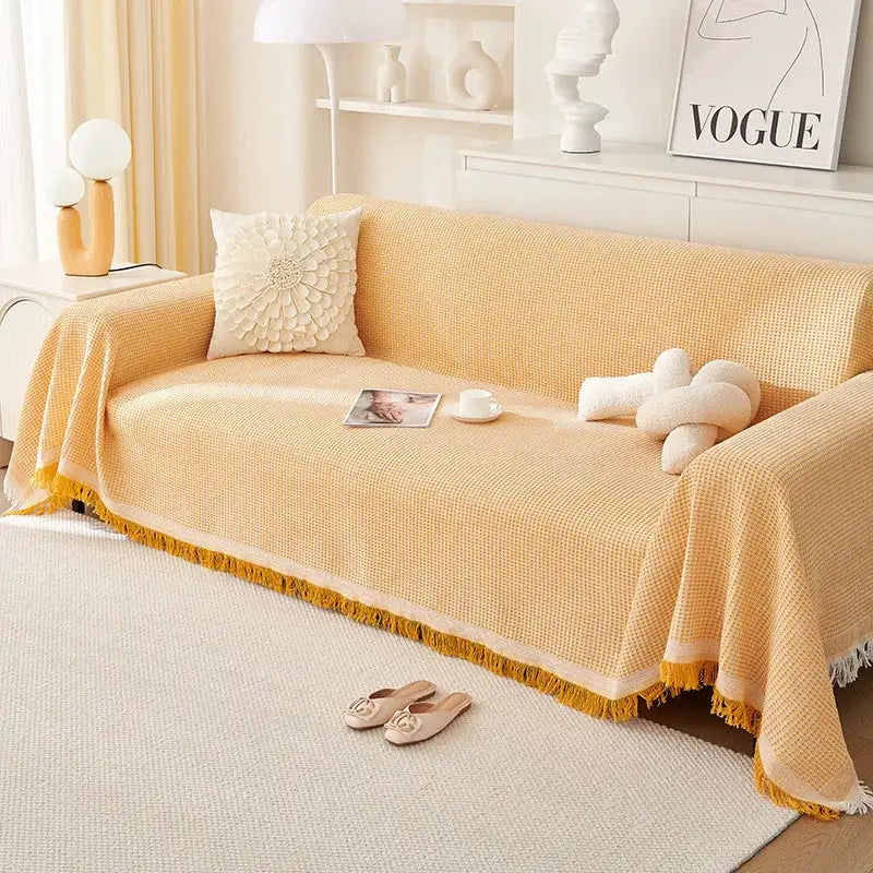 Sofa cover in cream wind-cotton yarn with fringe, full-coverage universal sofa protector on a yellow-beige couch.