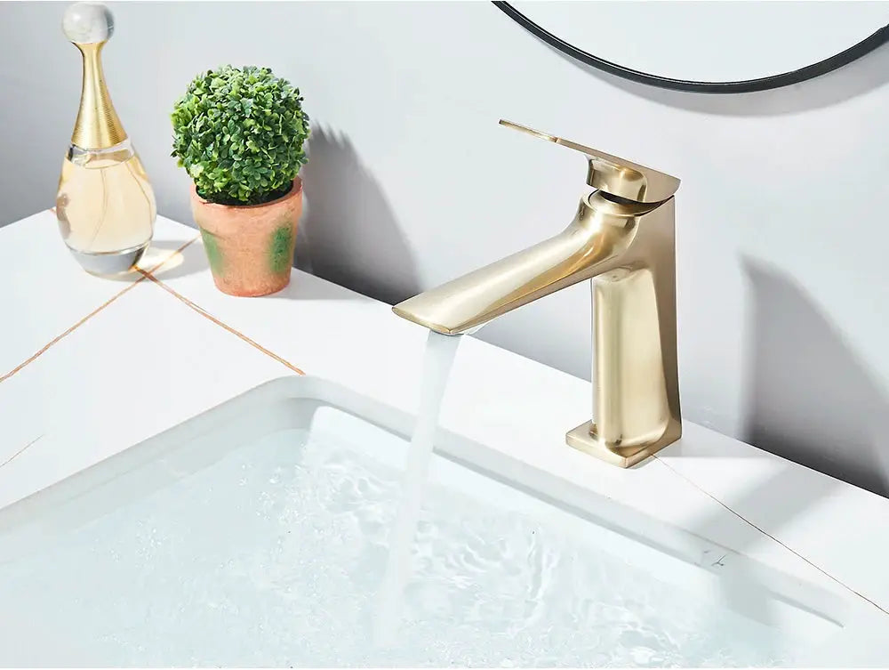 Brushed gold deck-mounted bathroom sink faucet with single-lever mixer, flowing water into a white basin.