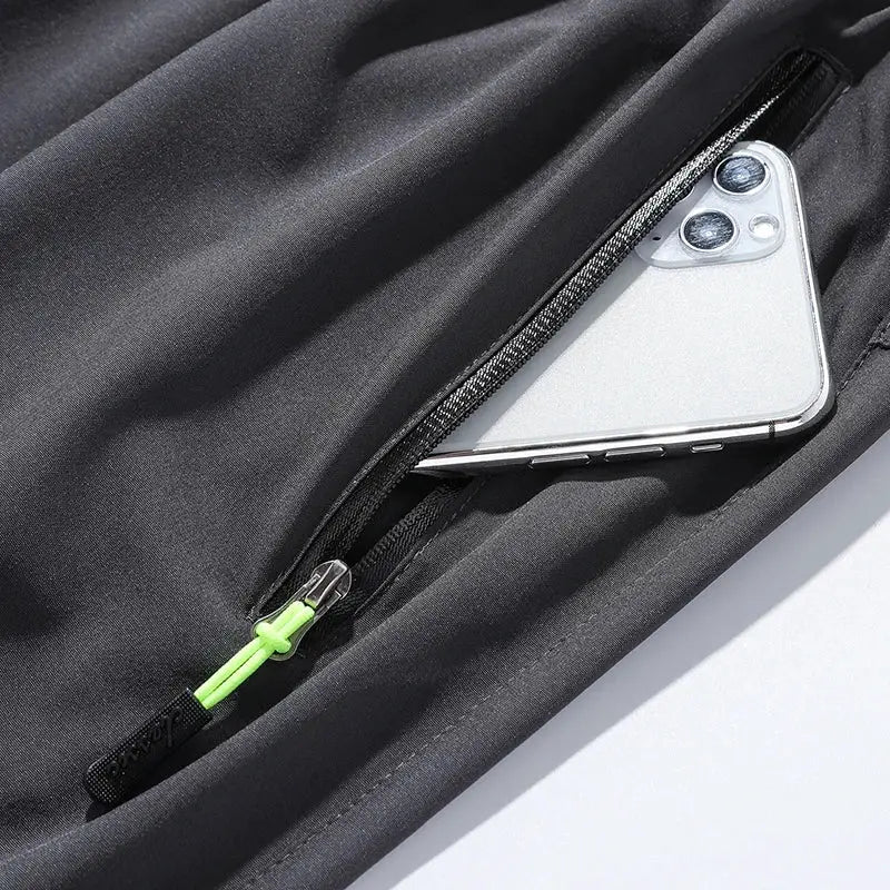 Men's black jogger pants with zip pocket and neon-green zipper pull, phone in pocket