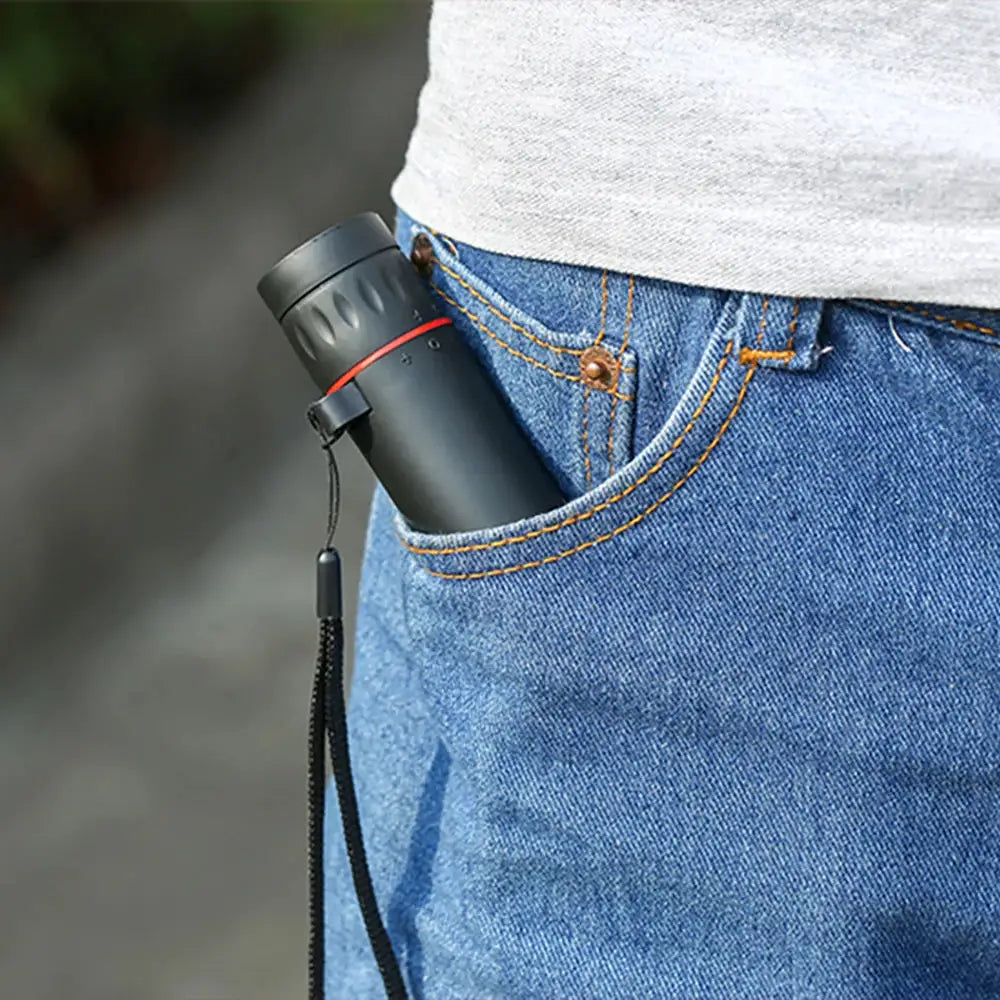 Monocular telescope in black with a red ring, tucked into a jeans pocket with a lanyard.