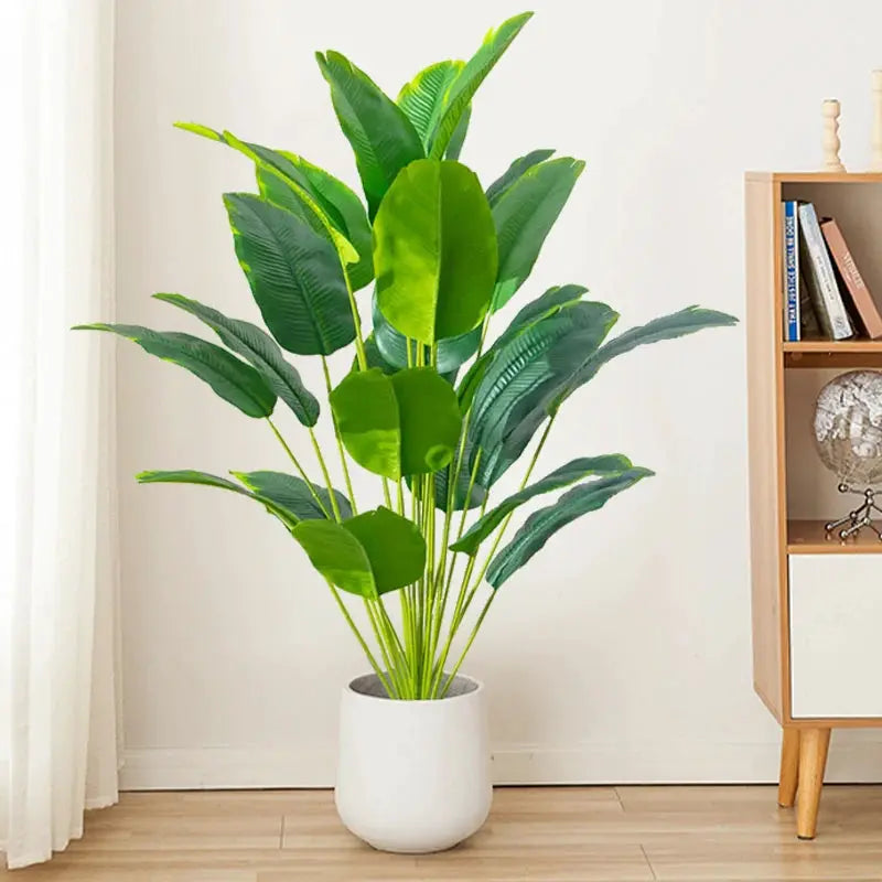 Artificial tropical plant with large green plastic leaves in a white pot.