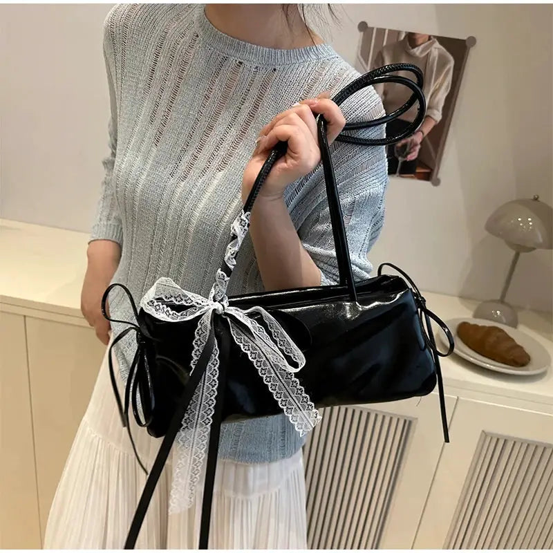 Black PU square shoulder bag with white lace bow, carried by a woman in a light blue knit sweater.