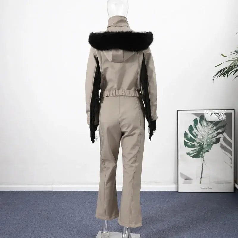 Beige one-piece ski suit with faux-fur hood, waist belt and black tassel sleeves.