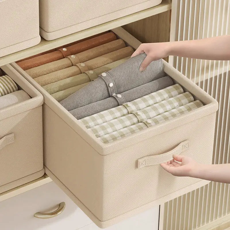 Beige fabric clothes organizer storage box with handle, storing rolled garments in a wardrobe