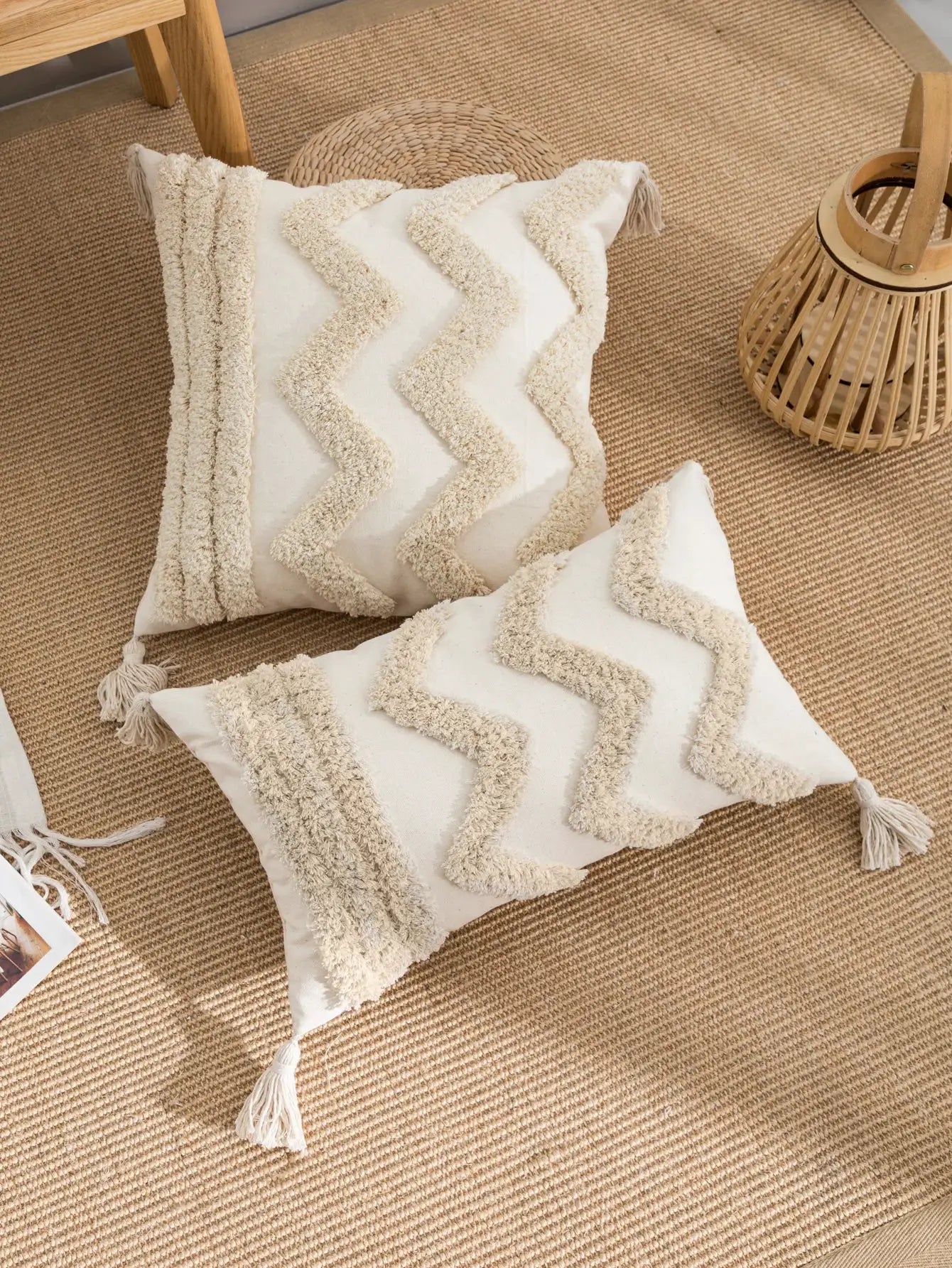 Two beige decorative pillows with cream textured zigzag trim and tassels on a jute rug