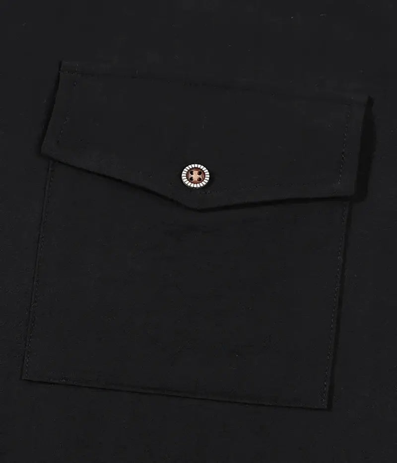 Men's black shirt pocket close-up with a flap and small metallic button.