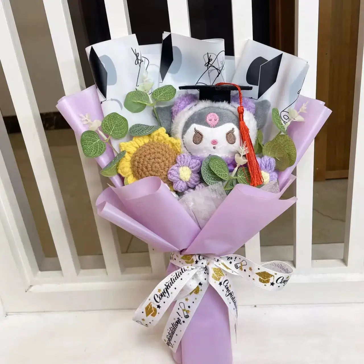 Stuffed plants bouquet with lavender wrap, sunflower and purple blooms, and a gray plush character in a graduation cap