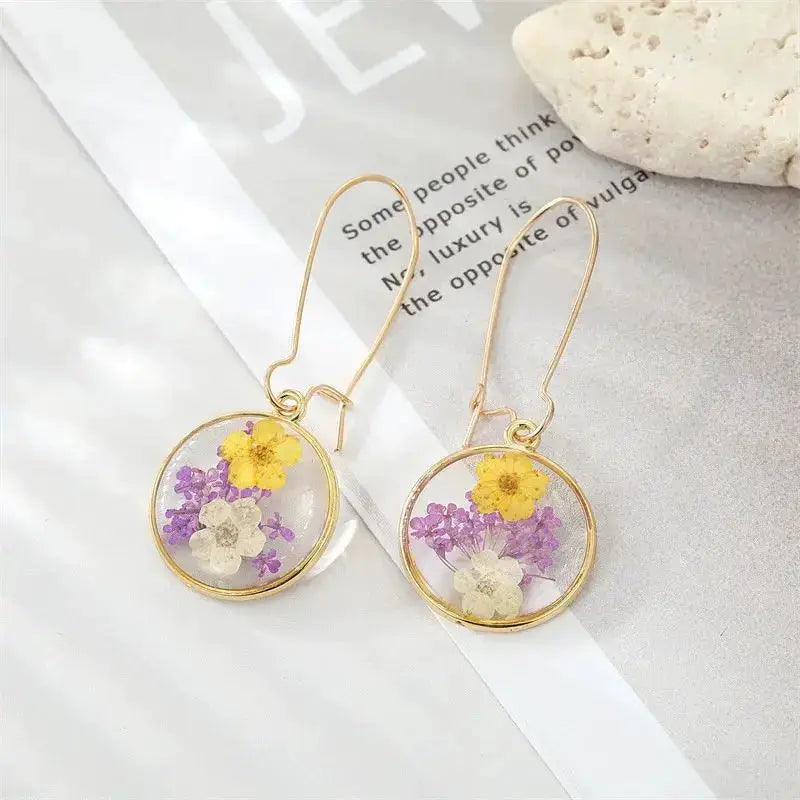 Pressed flower epoxy resin dangle earrings with colorful yellow, purple, and white blooms on gold-tone hoops