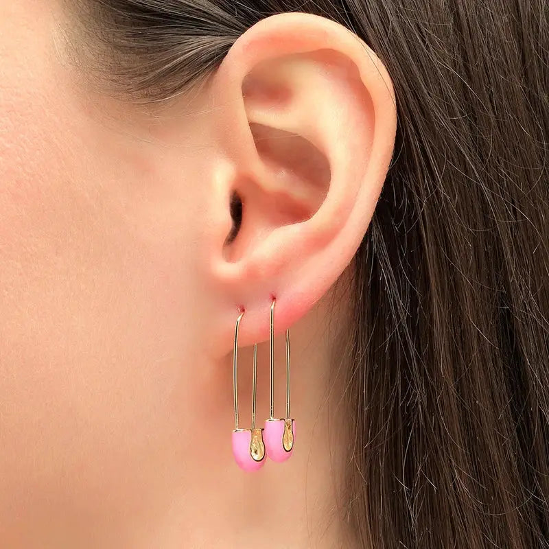 Pair of gold-tone hoop earrings with pink semicircle pendants worn on the ear