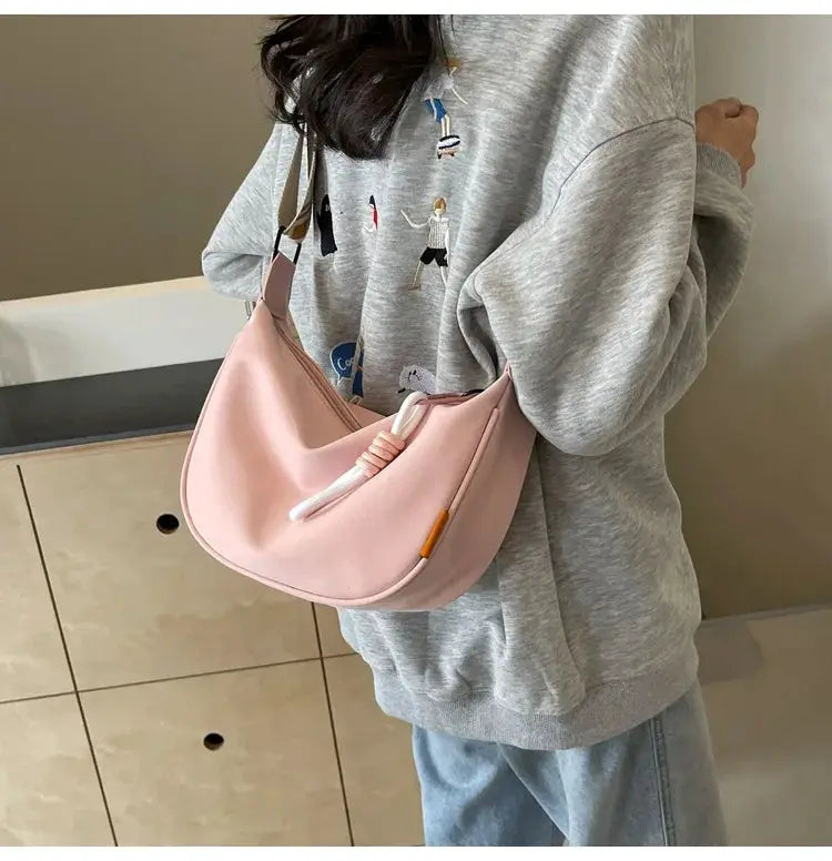 Pink dumpling-style crossbody bag with a wide shoulder strap, worn by a person in a gray hoodie.