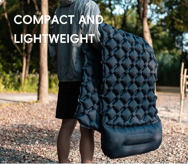TARKA inflatable camping mat with pillow; dark blue quilted air mattress carried by a person outdoors.