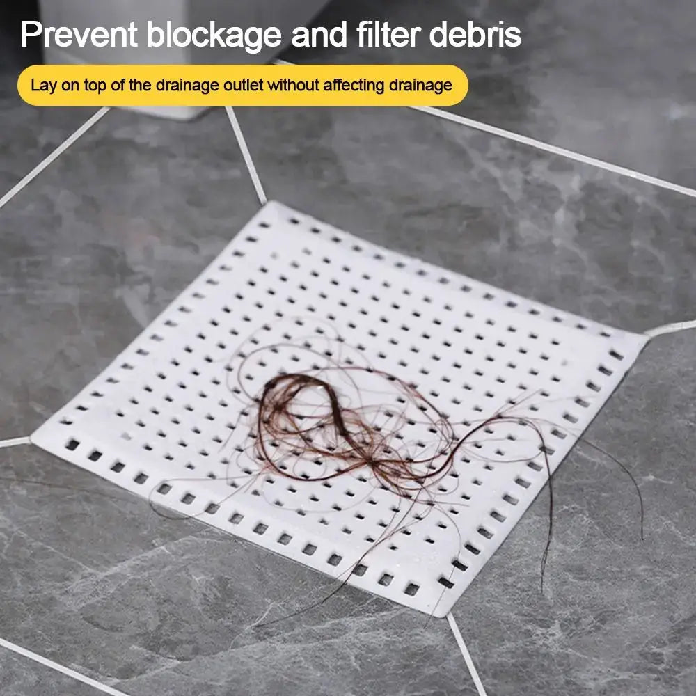 Simples Market drain strainer pad, white perforated square with hair debris on gray tile