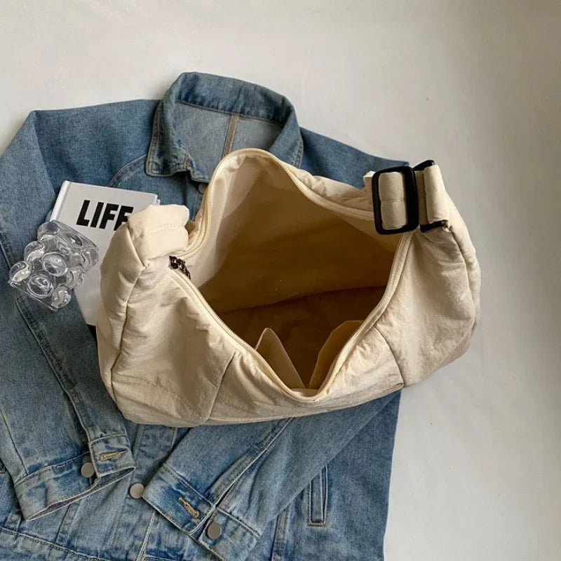 Beige cloth crossbody bag with zipper, roomy interior, shown on a blue denim jacket.