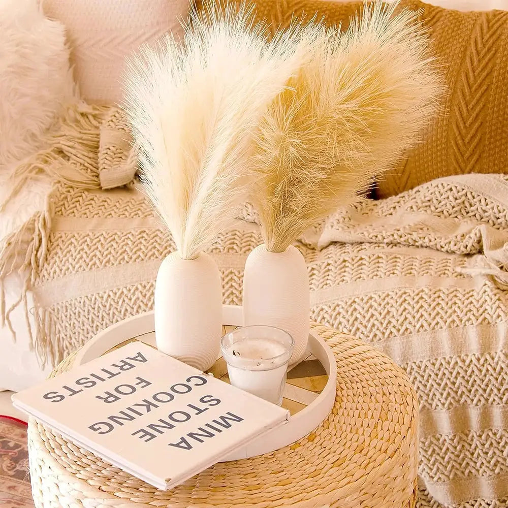 Fluffy pampas grass bundles in two white vases on a round woven table, beige Boho decor, home decor scene.