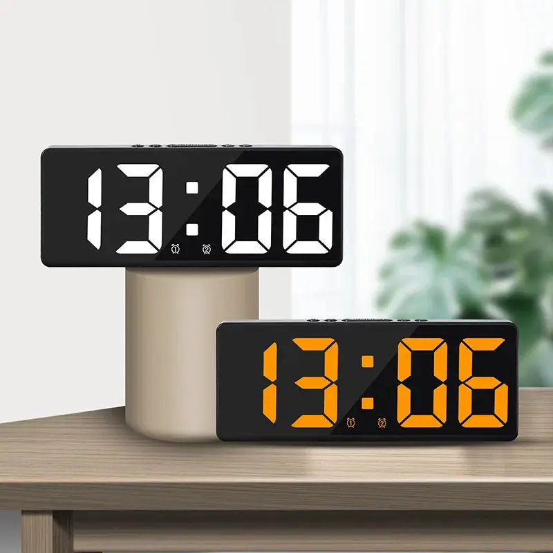 Two Simples Market acrylic mirror digital alarm clocks with large white and orange LED displays on a desk