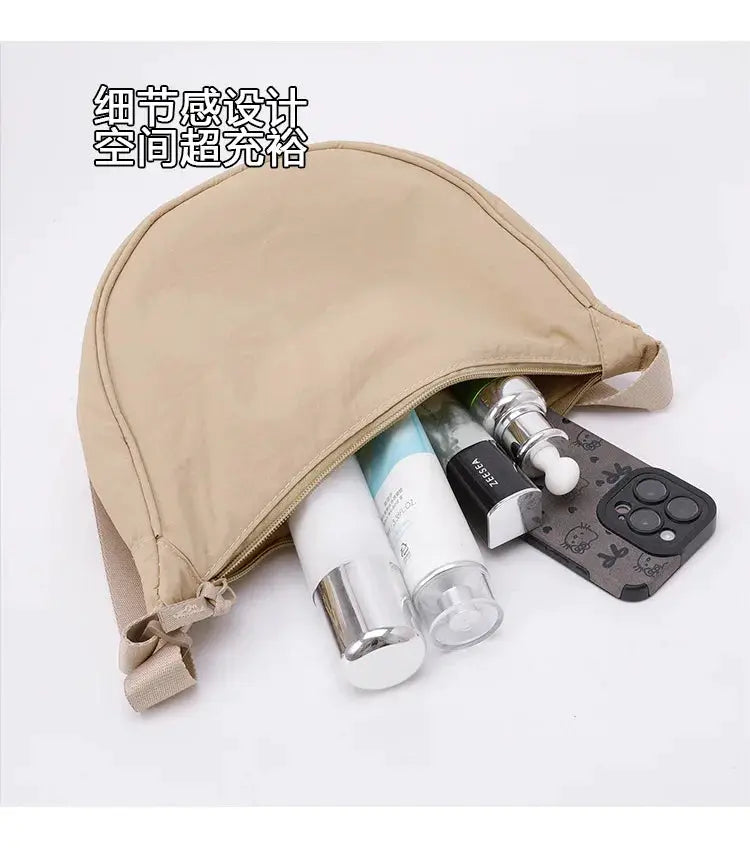 Beige nylon crescent crossbody bag with large capacity, holding several cosmetics and a smartphone