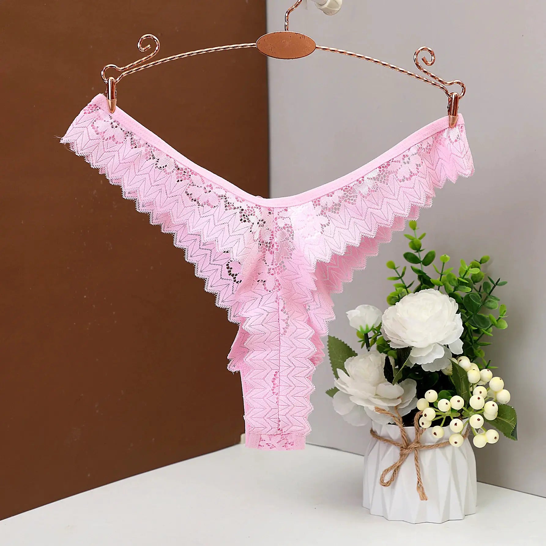 Pink lace thong underwear, low-rise with scalloped edges, hanging on a copper hanger