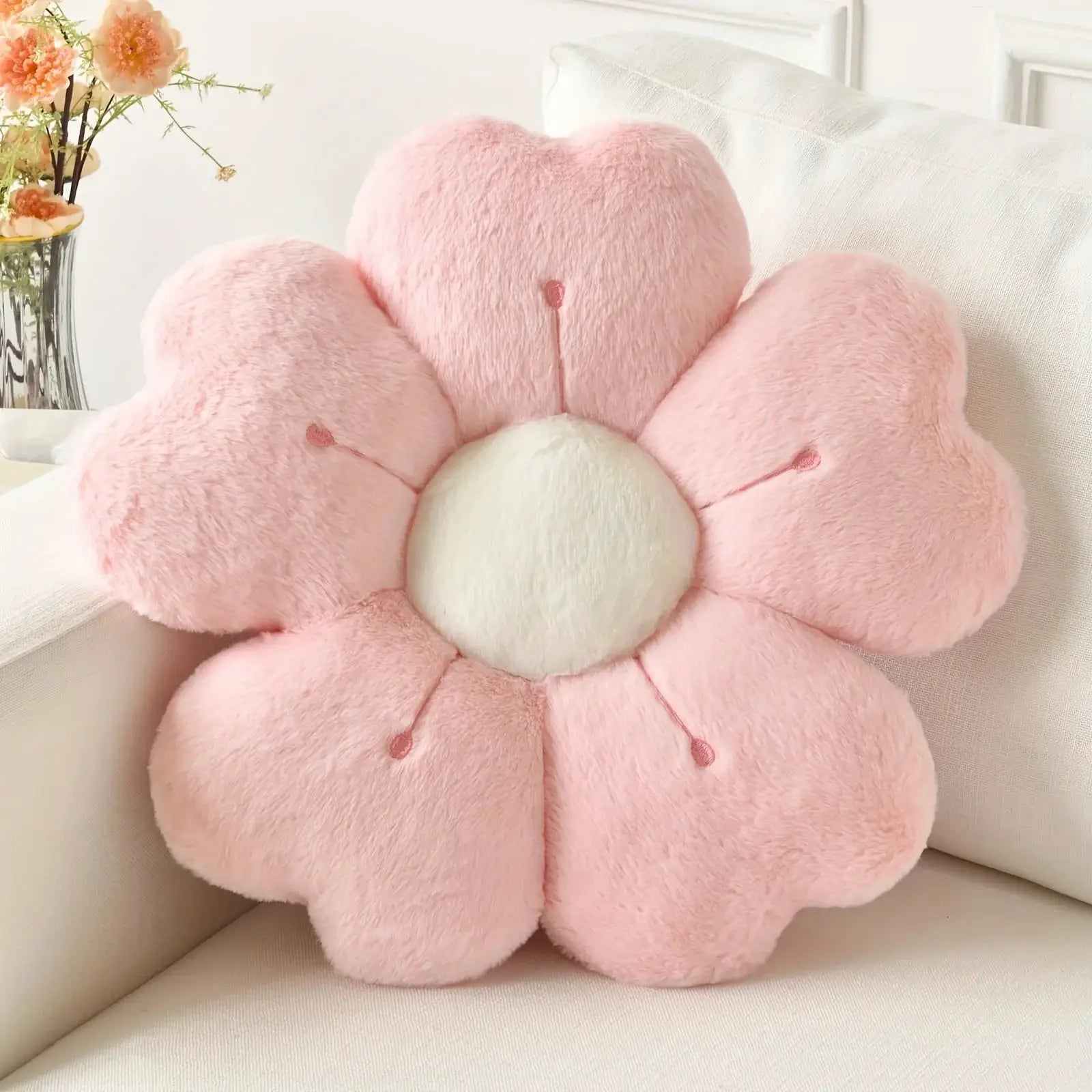 Flower-shaped plush throw pillow, pink with white center, decorative cushion on a white sofa by Simples Market.
