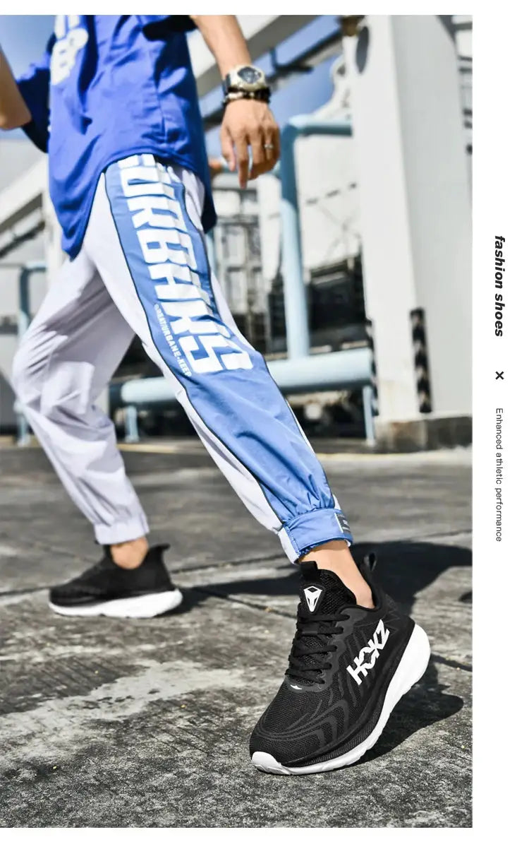 Pair of black HOKA running shoes with white soles and breathable mesh on a person wearing blue and white joggers.