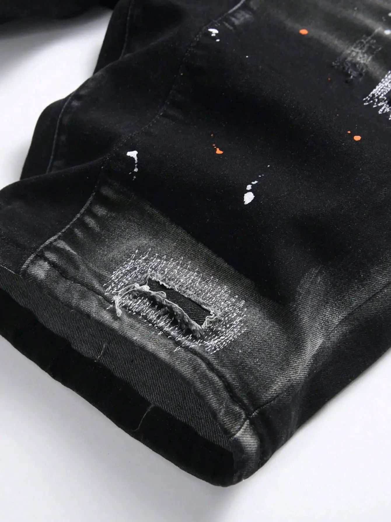 Men's black denim shorts with ripped details, orange paint splatters, knee-length rolled cuffs