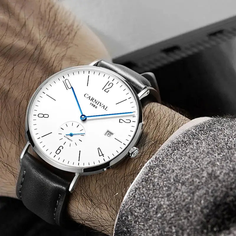 Carnival men's dress watch with white dial, blue hands, seconds subdial, date window, silver case, black leather strap.