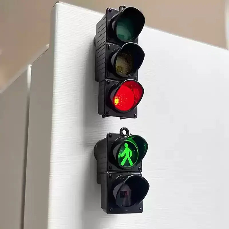 Two traffic light refrigerator magnets; miniature black signal units with red and green lenses