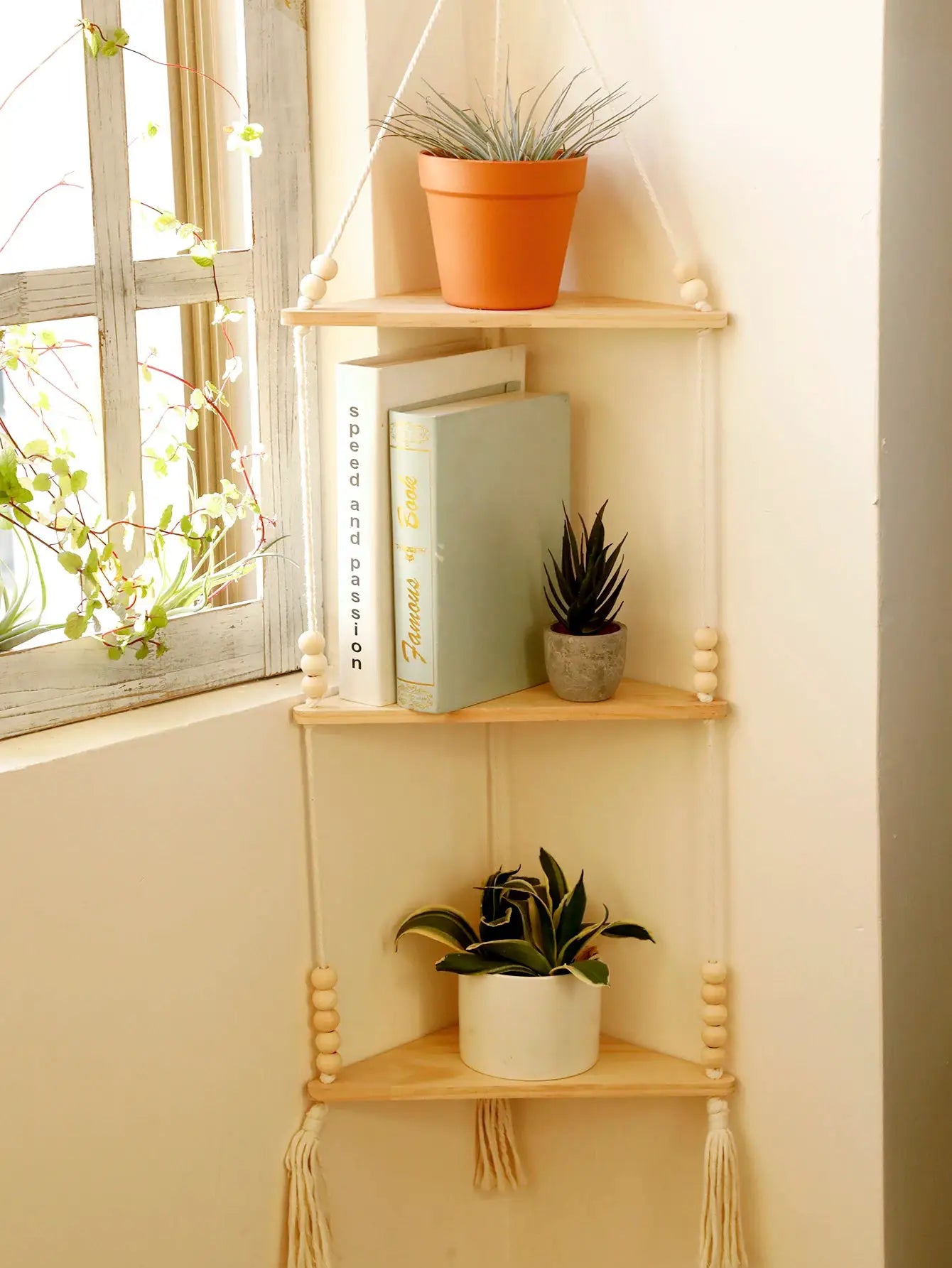 Three-tier wooden triangle corner wall shelf with rope hanger, displaying potted plants and books