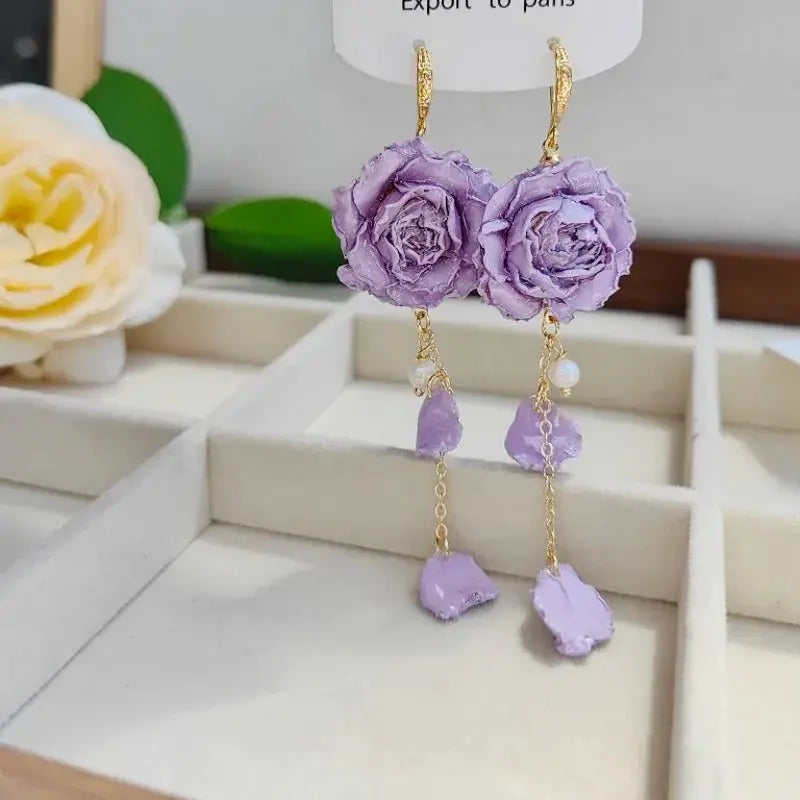 Pair of Immortal Rose long earrings by Simples Market; purple epoxy roses with gold chains and lavender stones.