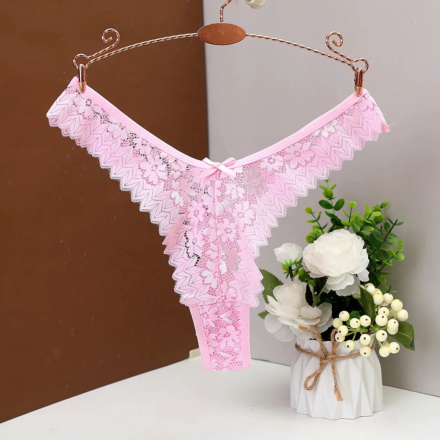Women's pink lace thong underwear, low-waist design with scalloped edges and bow detail.