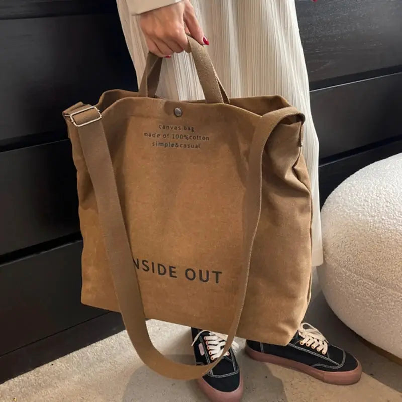 Brown canvas cross-body bag with a long adjustable strap and short handles; large-capacity tote.