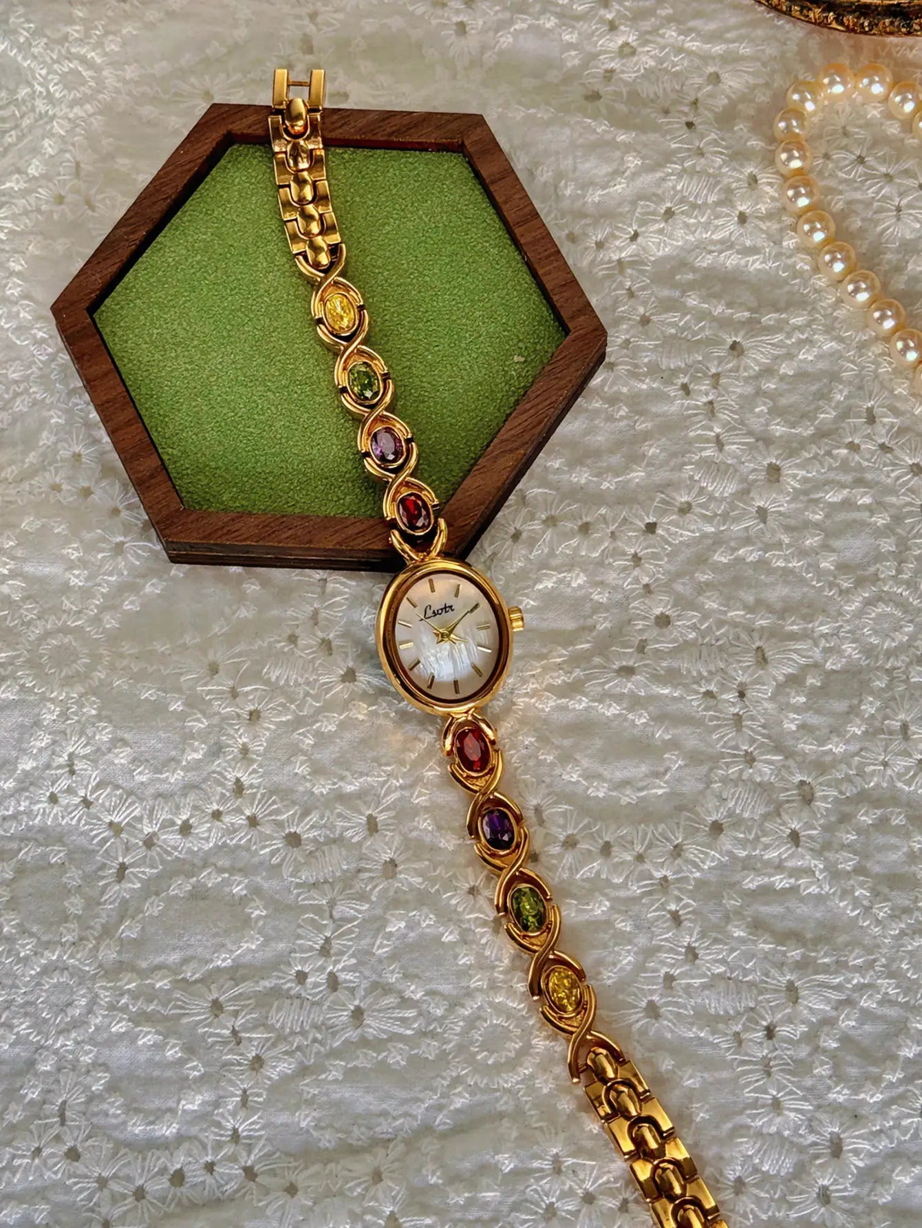 Simples Market gold-tone women's luxury watch with tourmalines and diamonds, oval mother-of-pearl dial; pearl necklace.
