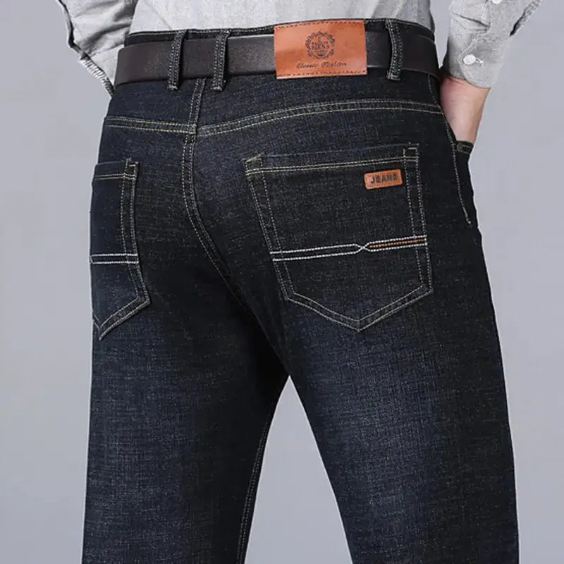 Men's dark denim jeans back view with two back pockets, contrast stitching, and a brown leather patch.