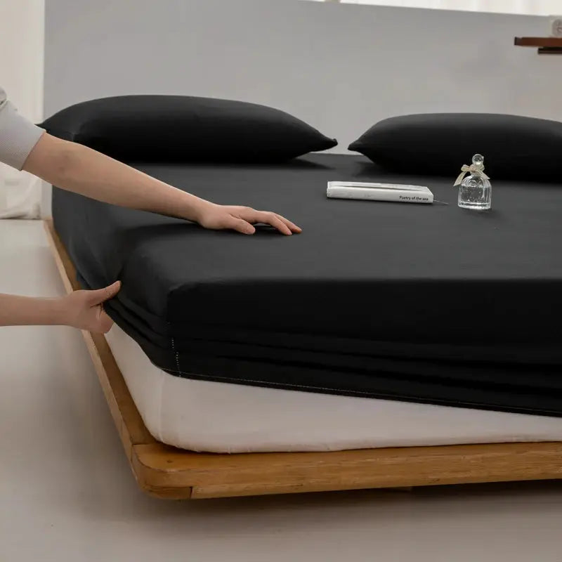 Soft cotton fitted sheet, black, with elastic band, on a white mattress atop a wooden bed frame
