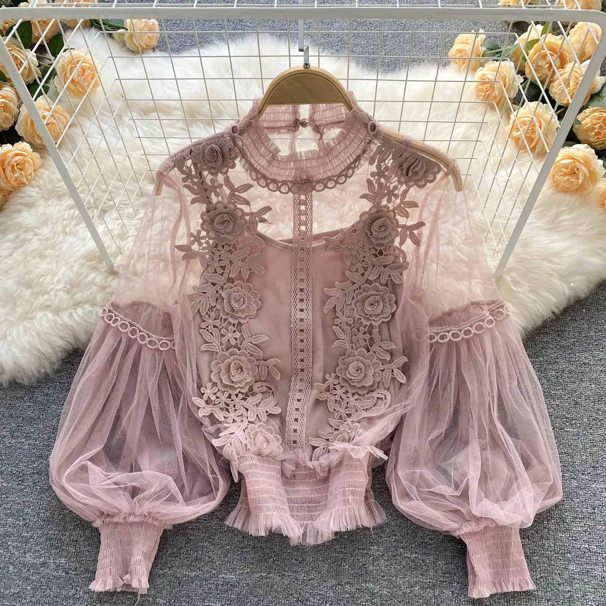 Pink lace puff-sleeve blouse with floral appliqués on sheer fabric, displayed on a wooden hanger.