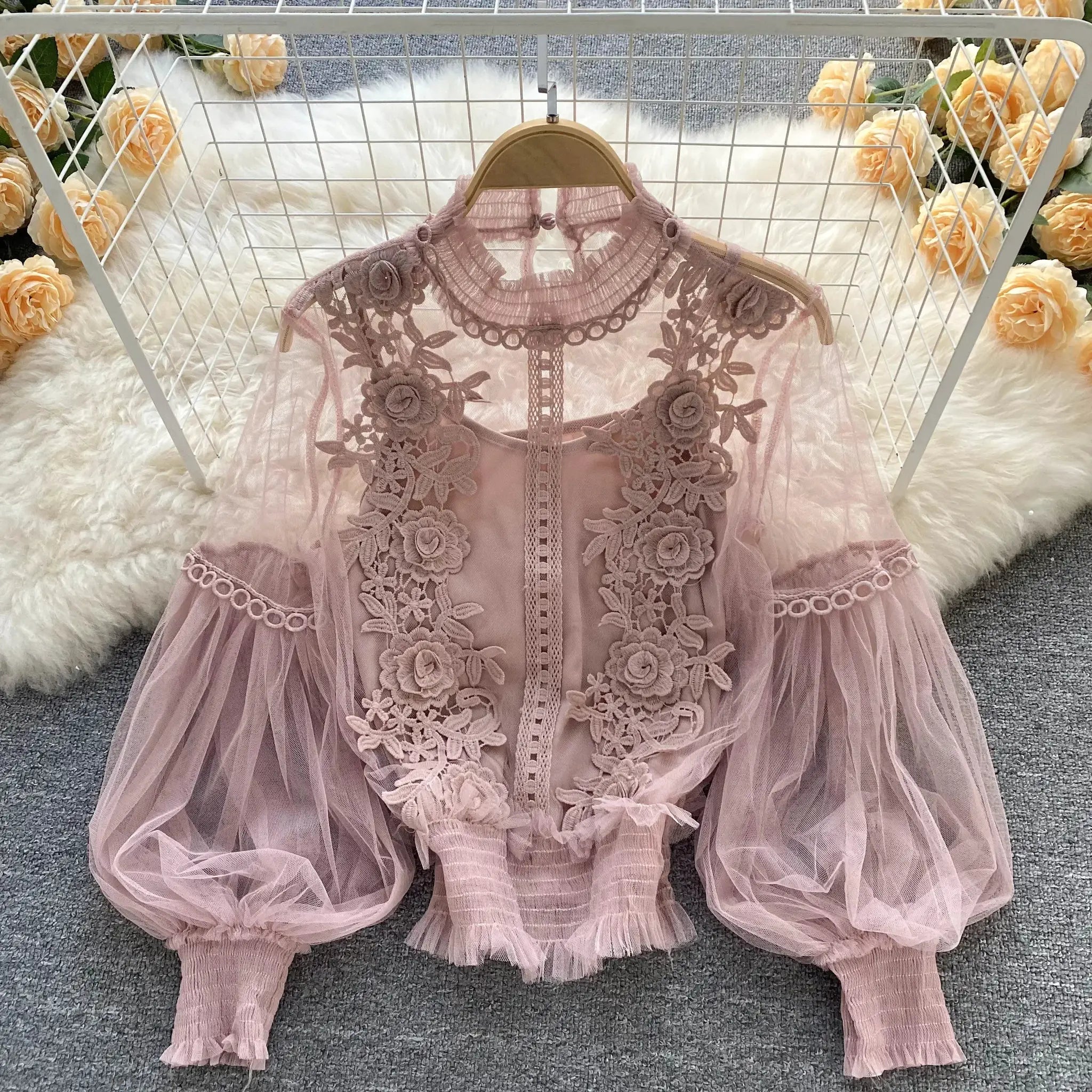 Pink lace puff-sleeve blouse with floral appliqués on sheer fabric, displayed on a wooden hanger.