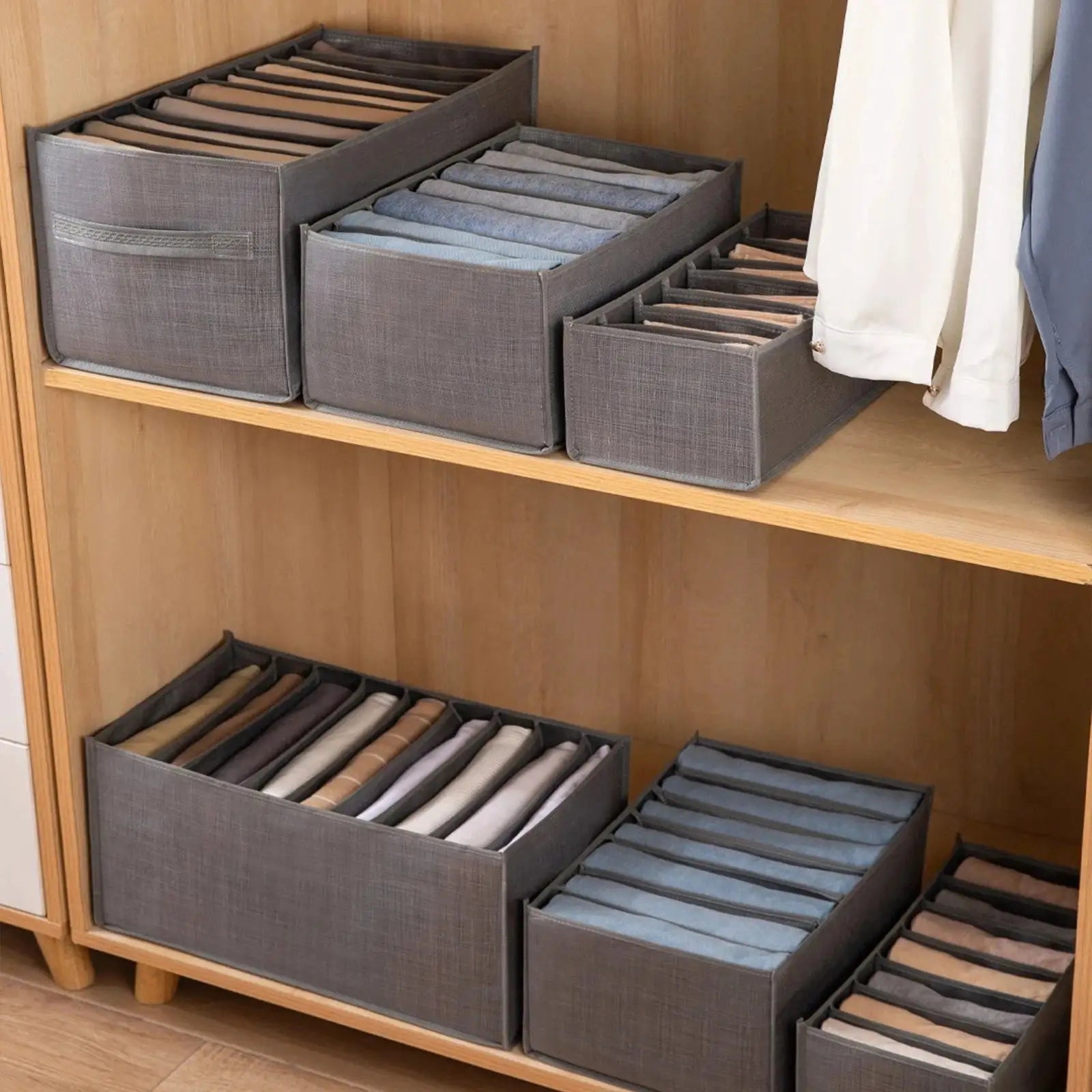 Gray fabric clothes organizer boxes with divided compartments on a wooden wardrobe shelf