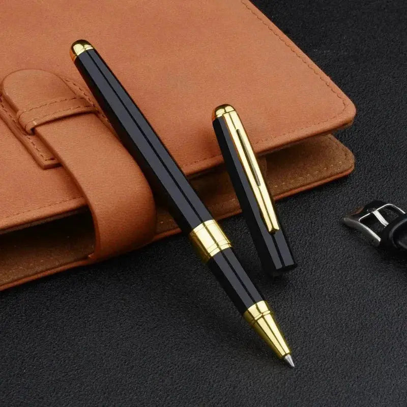 Ballpoint pens, two black with gold-tone caps and tips on a tan leather notebook.