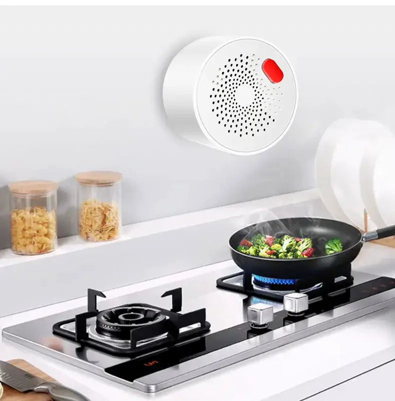 White circular gas leak detector with red indicator mounted above a gas stove in kitchen